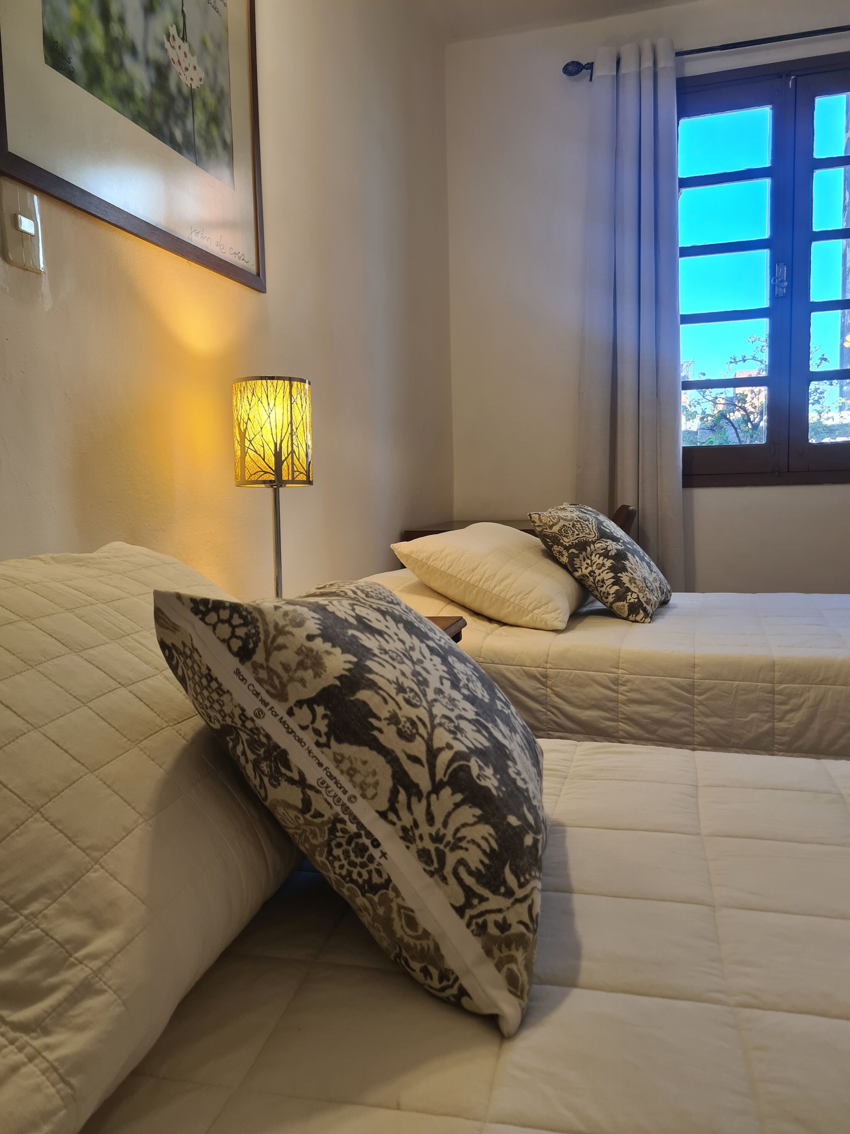 Un dormitorio con dos camas, una mesita de noche, una lámpara y una ventana con cortinas.