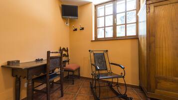 Una habitación con escritorio de madera, dos sillas, televisor montado en la pared y ventana con vista al exterior.