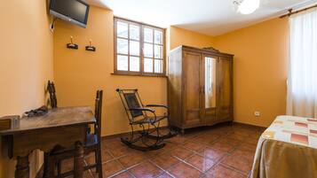 A room with a wooden table, a rocking chair, a cabinet, a television mounted on the wall, and a window with curtains.