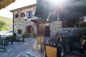 A stone building with a patio area featuring outdoor seating and a large umbrella. - Hotel rural Valle de Ancares (Candin)