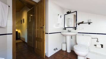 Un baño con puerta de madera, azulejos blancos, un lavamanos, un inodoro y un espejo.