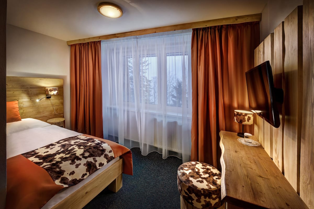 Een hotelkamer met een bed, een houten bureau, een stoel, een televisie en een raam met gordijnen.
