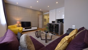 A modern living room with a sofa set, a coffee table, a flat-screen TV, and a kitchen area in the background. - Boutique Rooms (Belgrade)