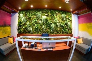 A reception desk with a glass top, surrounded by a modern interior with a green wall and a sofa. - Boutique Rooms (Belgrade)