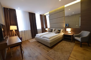 A modern hotel room with a large bed, bedside tables, a desk, and a chair.