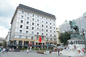 A multi-story hotel with a modern facade, outdoor seating area, and a statue in the foreground.