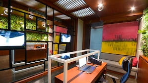 A modern office space with a glass desk, a laptop, a chair, a sofa, and a wall with a green plant wall and a painting. - Boutique Rooms (Belgrade)
