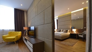 A modern hotel room with a sofa, a TV, a bedside table, a lamp, and a bed with a nightstand. - Boutique Rooms (Belgrade)