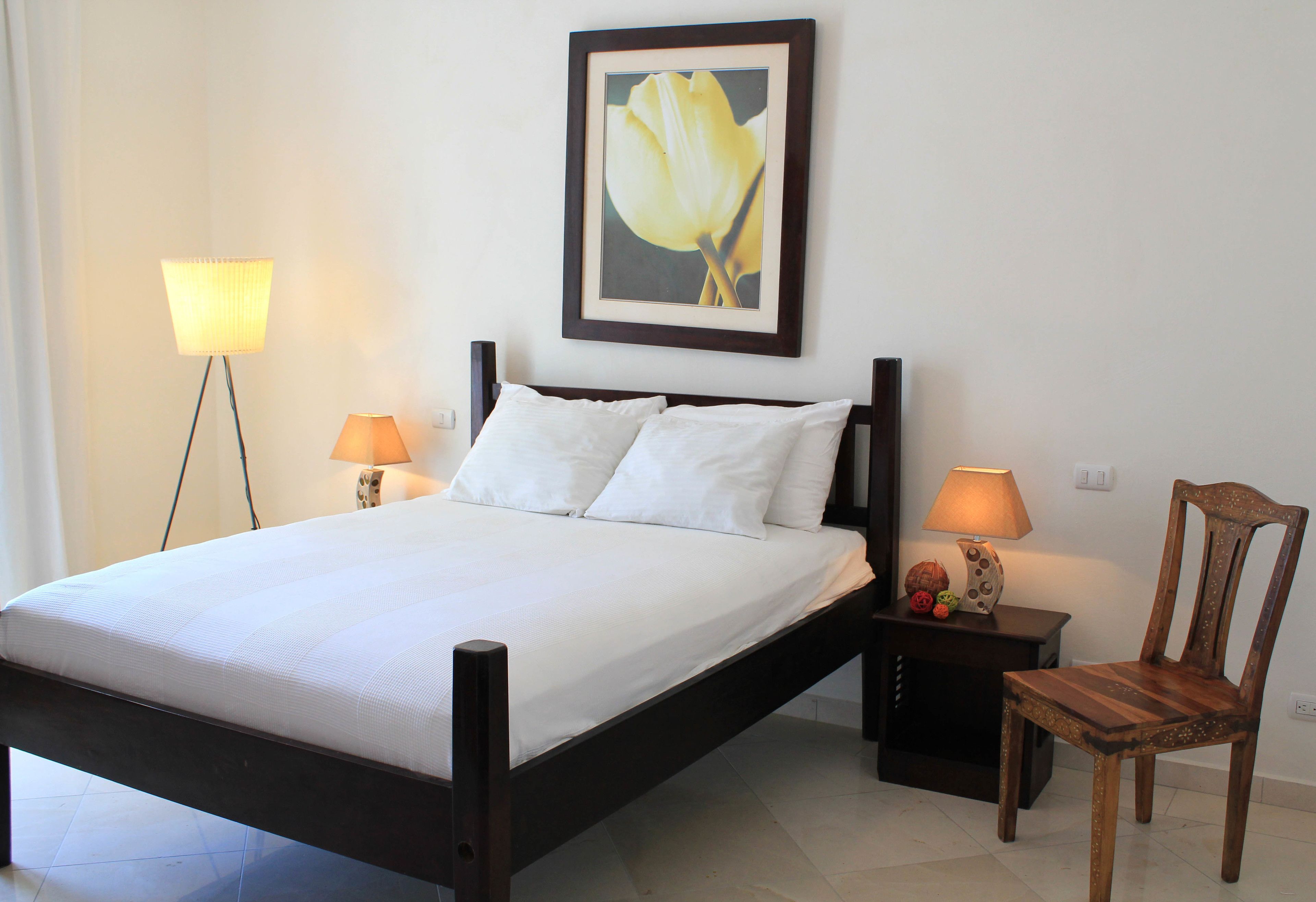 A neatly made bed with white linens, a wooden headboard, and two bedside lamps.