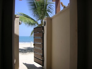 A doorway leading to a beach with a palm tree and a gate. - Beach Palace Cabarete (Cabarete)
