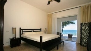 A bedroom with a bed, bedside lamps, a ceiling fan, a view of the ocean, and a beach outside. - Beach Palace Cabarete (Cabarete)