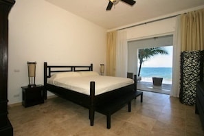A bedroom with a bed, bedside lamps, a ceiling fan, a view of the ocean, and a beach outside. - Beach Palace Cabarete (Cabarete)