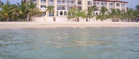 A beachfront hotel with multiple balconies, palm trees, and a sandy beach.