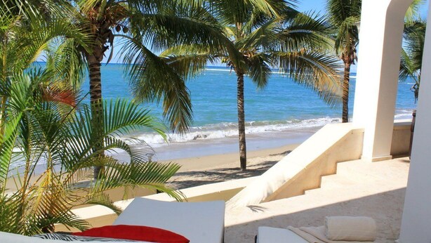 A beach view with palm trees, a staircase leading to the beach, and a lounge area with a bed and a chair. - Beach Palace Cabarete (Cabarete)
