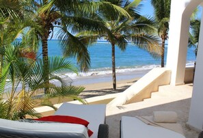 A beach view with palm trees, a staircase leading to the beach, and a lounge area with a bed and a chair. - Beach Palace Cabarete (Cabarete)