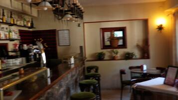 Una zona de bar con taburetes, una barra con botellas y un comedor con sillas y una mesa.