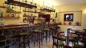 Una zona de bar con taburetes y mesas, una pared de piedra y estanterías llenas de botellas.