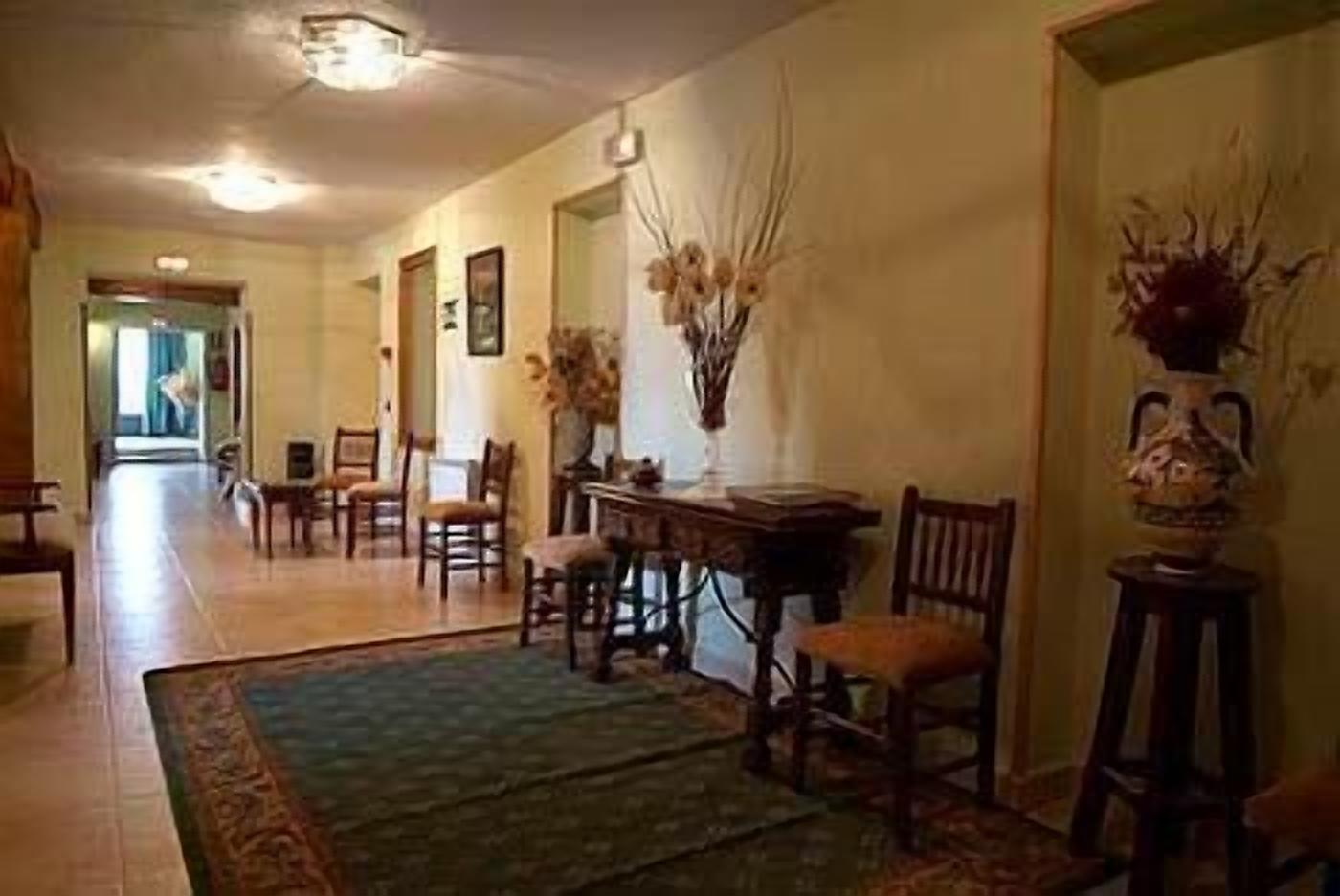 A hallway with a dining area featuring wooden chairs, a table, and a vase with dried plants.
