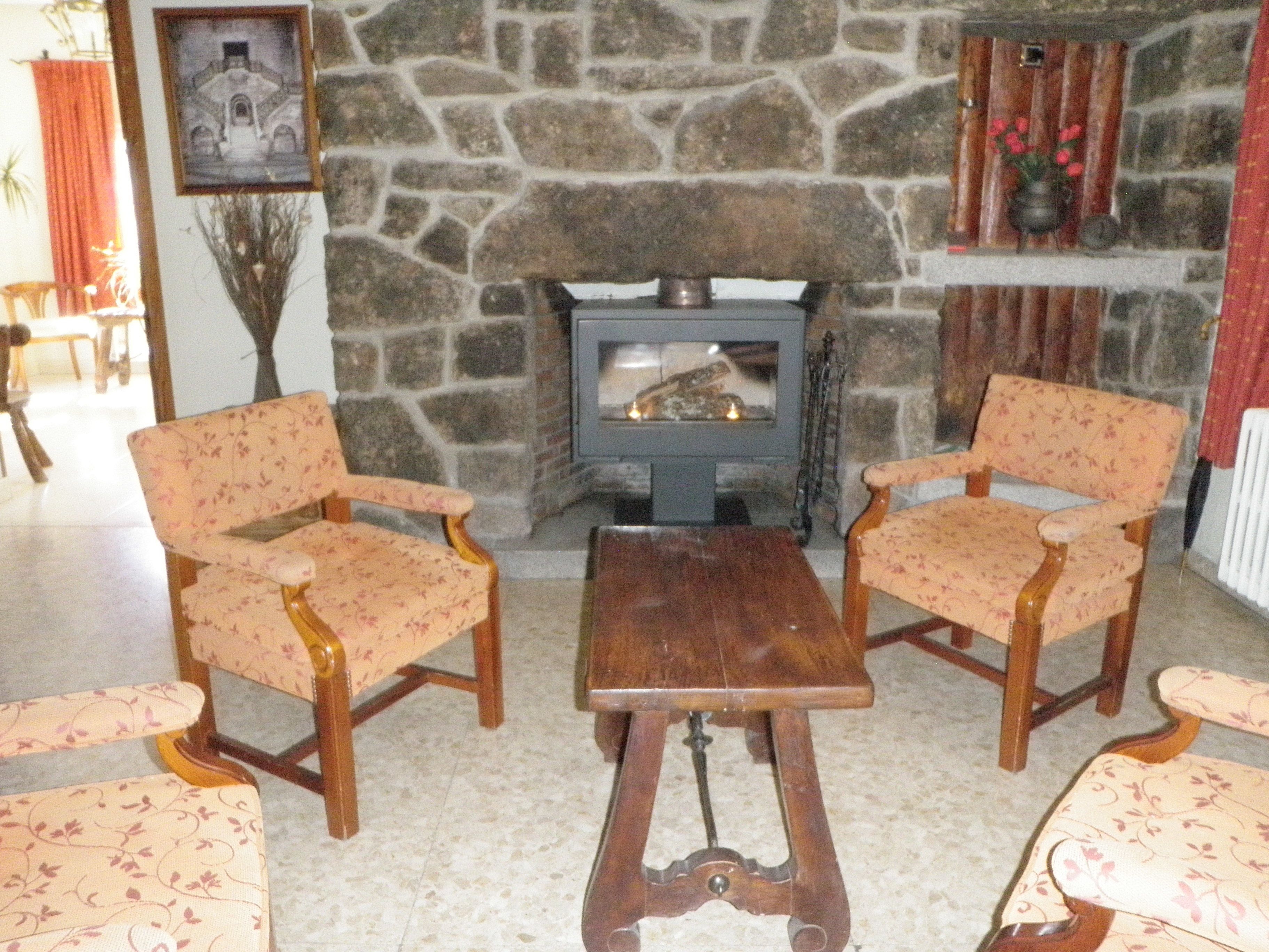 Un cuarto acogedor con una chimenea de piedra, dos sillones con estampado floral y una mesa de centro de madera.