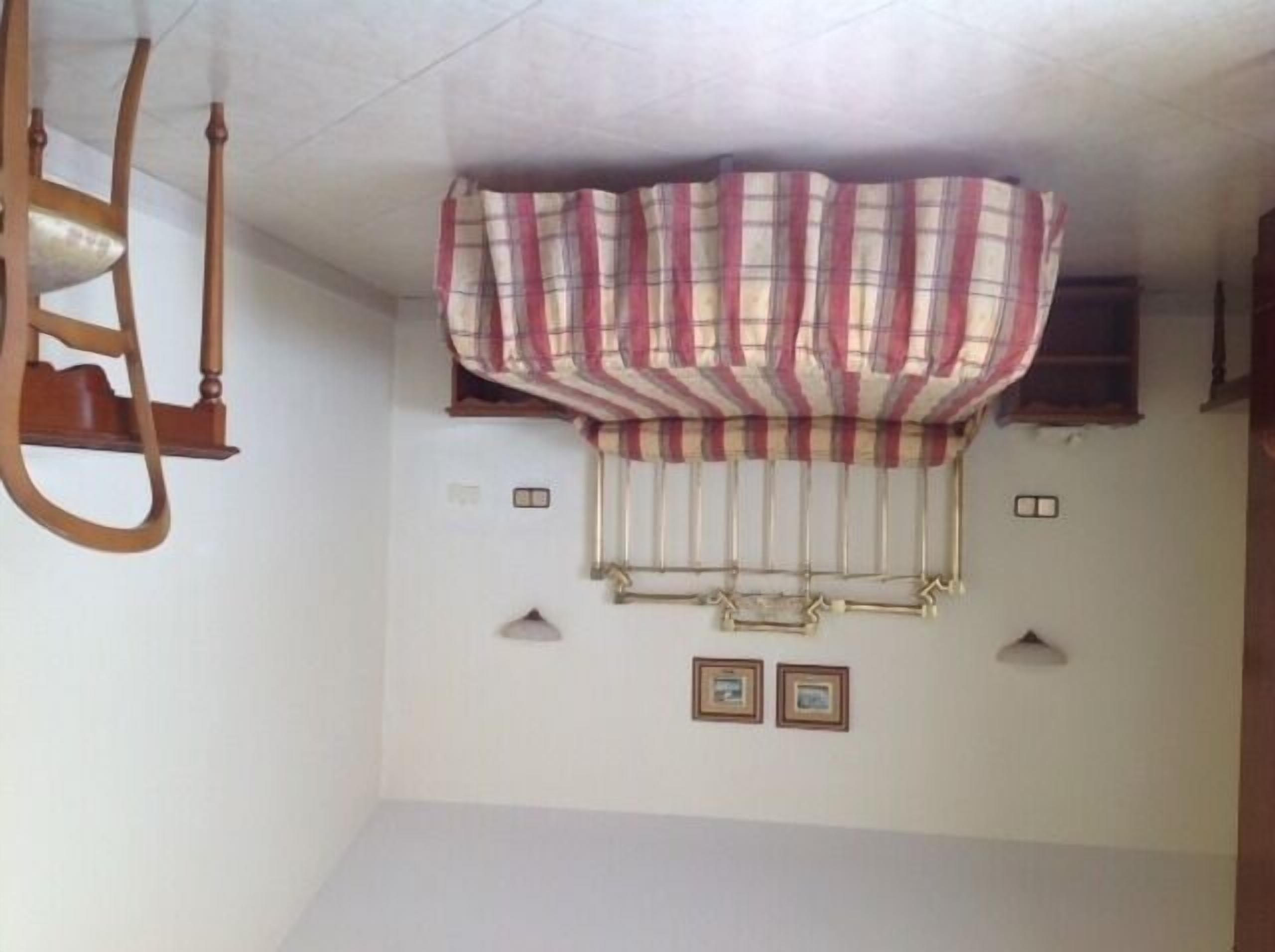 Una habitación con ventilador de techo, cortina escocesa y dos cuadros en la pared.