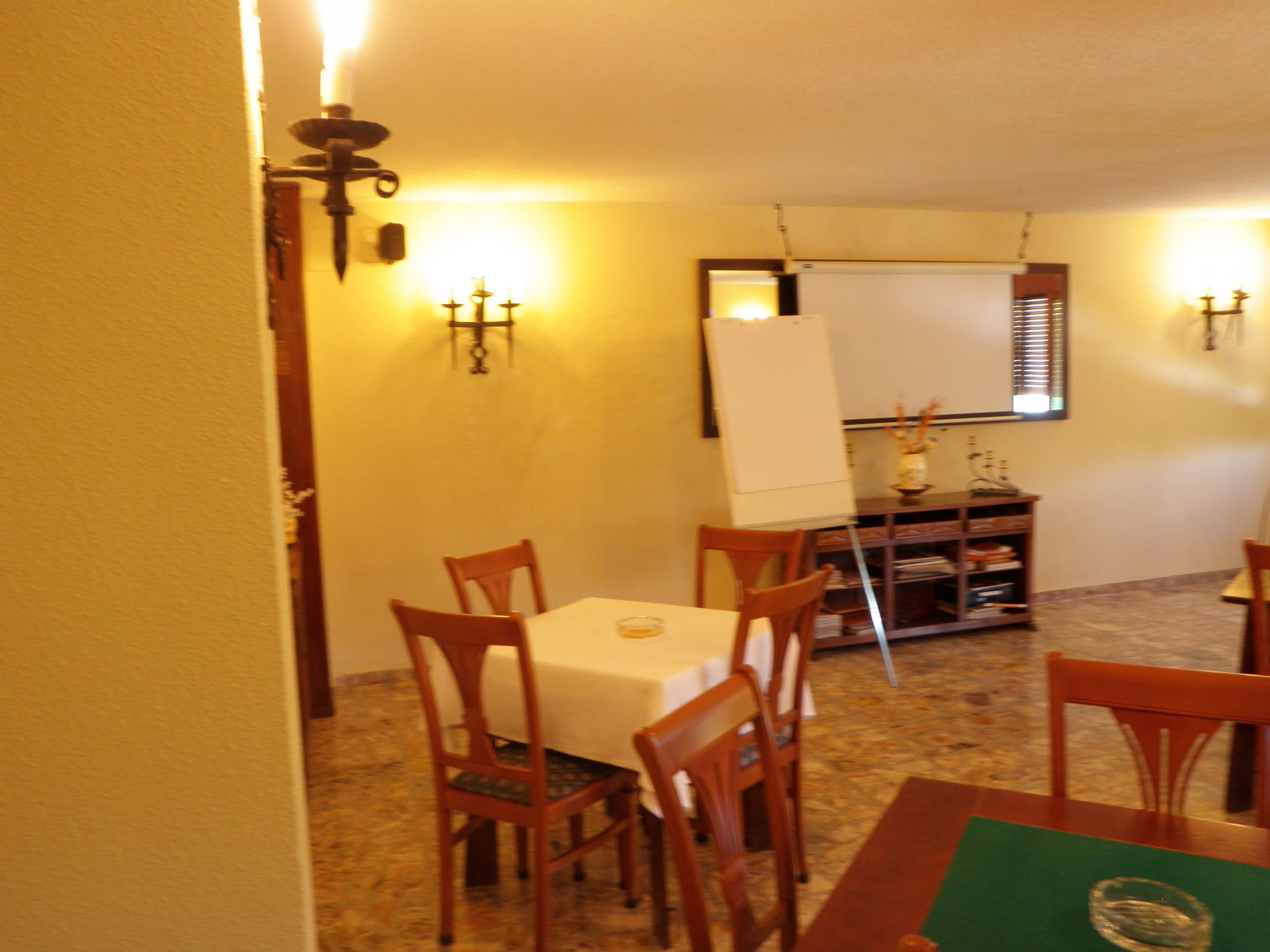 A dining area with a table set for two, a whiteboard on the wall, and a small cabinet with decorative items.