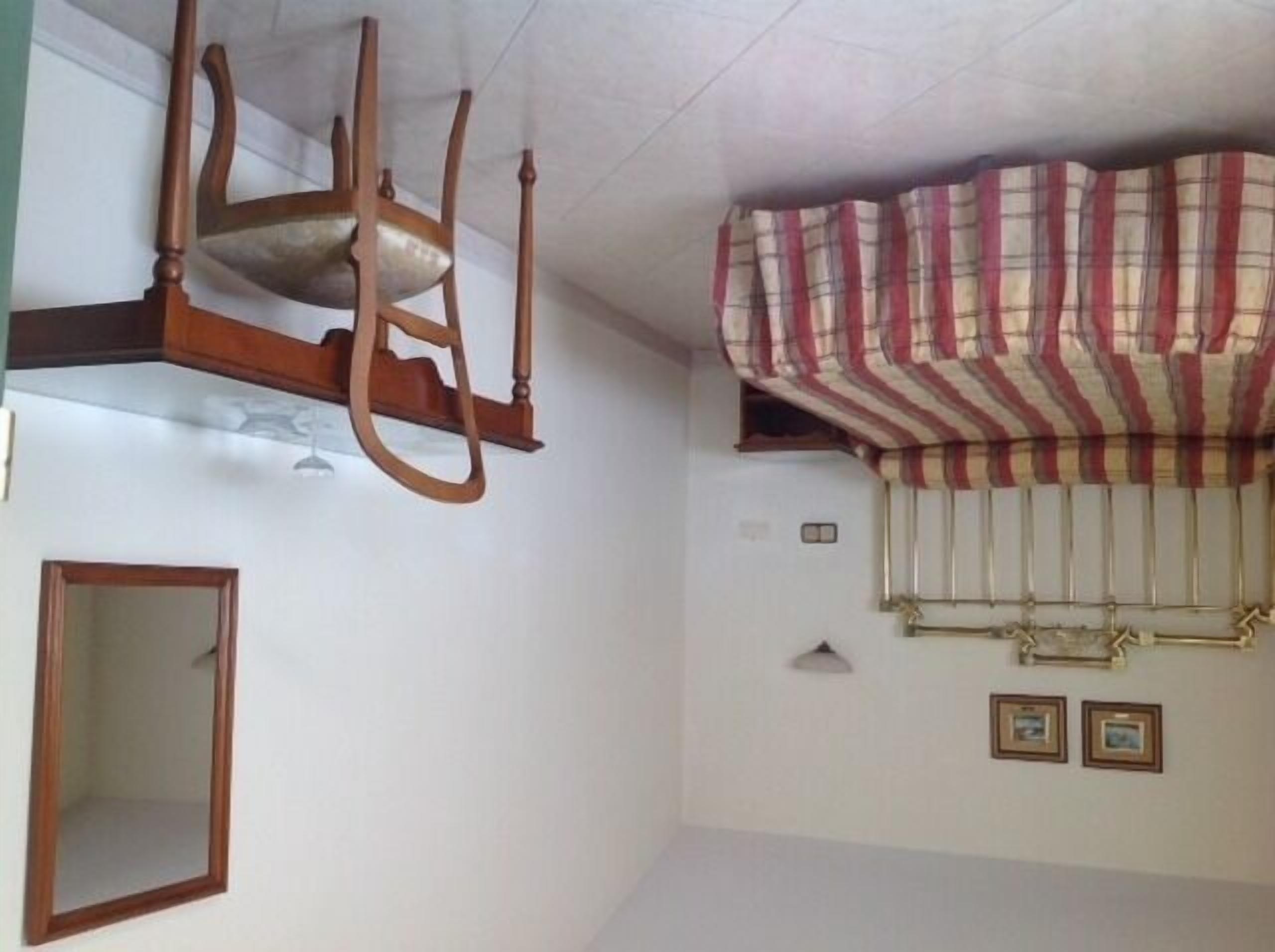 A room with a wooden chair, a mirror, and a striped curtain.