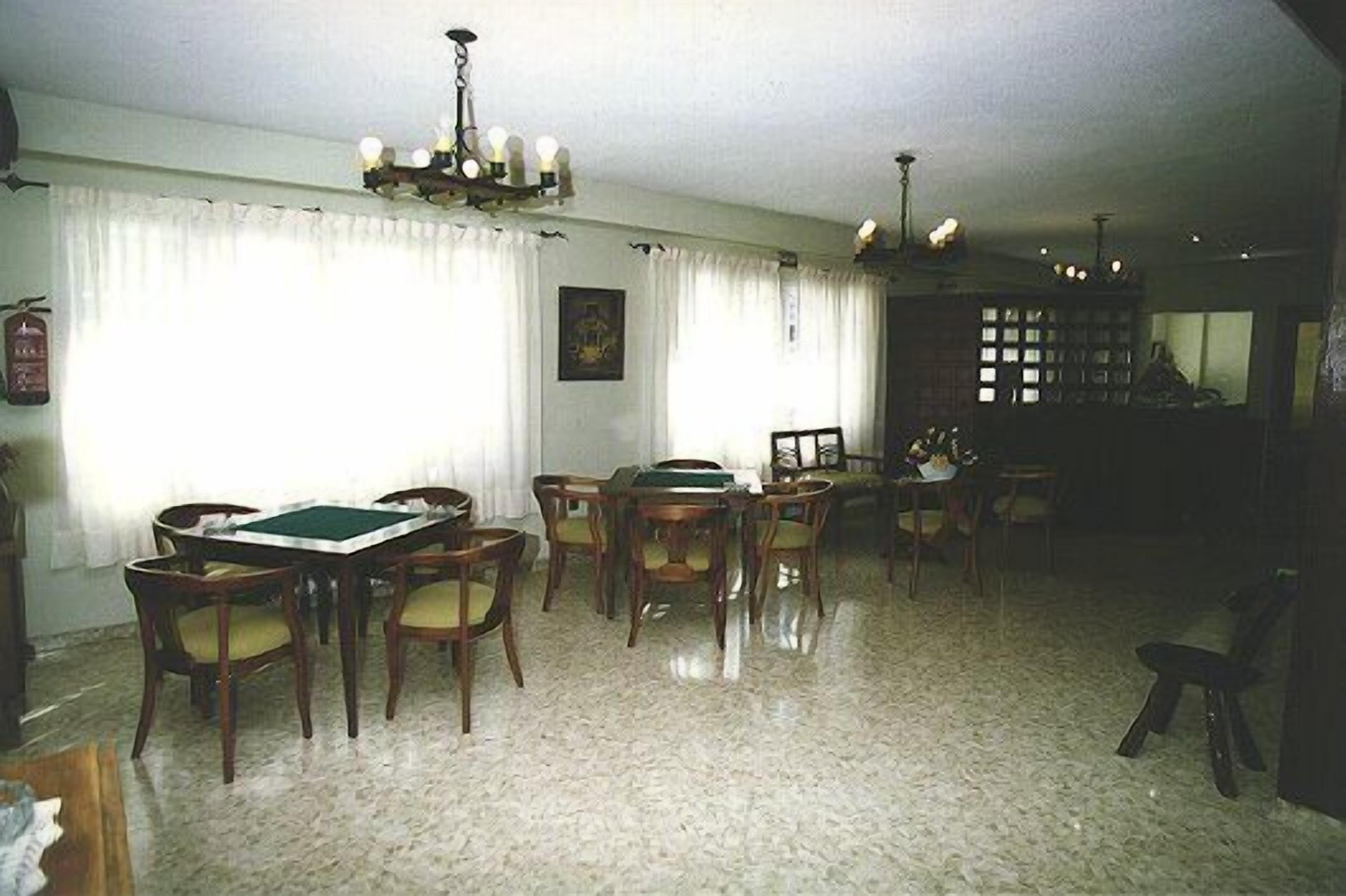 Uma área de refeições com uma mesa retangular e cadeiras, um lustre e uma estante de livros ao fundo.