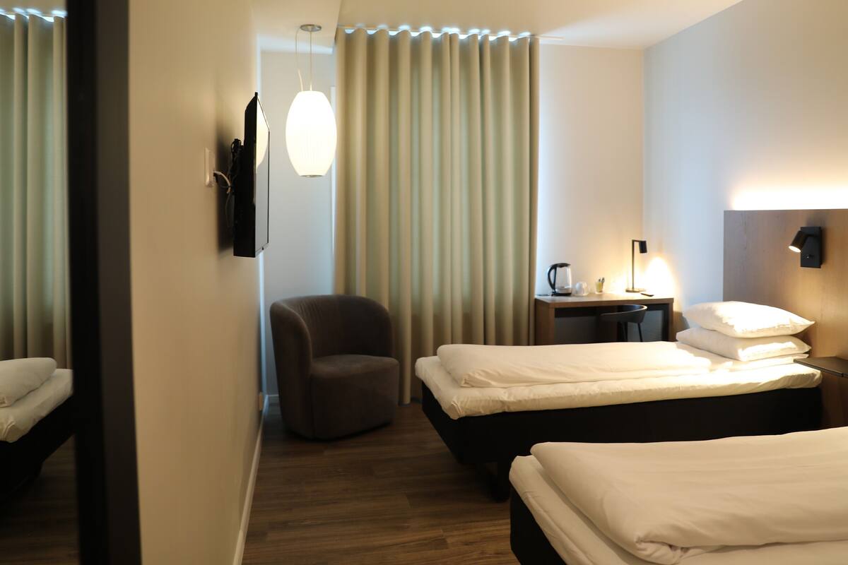 A hotel room with two beds, a desk, a chair, and a wall-mounted TV.