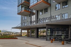 A modern hotel with a prominent entrance, outdoor seating area, and a view of the surrounding landscape.