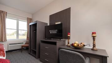 Habitación de hotel con televisión, escritorio con frutero, silla, armario y ventana con cortinas.
