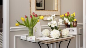 Un mostrador de recepción con superficie de vidrio, un jarrón blanco con tulipanes amarillos y rojos, un jarrón blanco con flores blancas y un letrero que dice 'Hagamos amigos'.