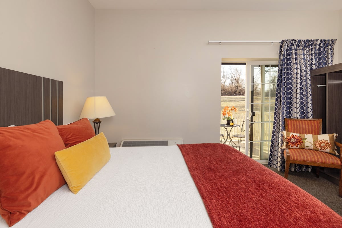 Quarto de hotel com uma cama, uma luminária, uma cadeira e vista através de uma porta de vidro.