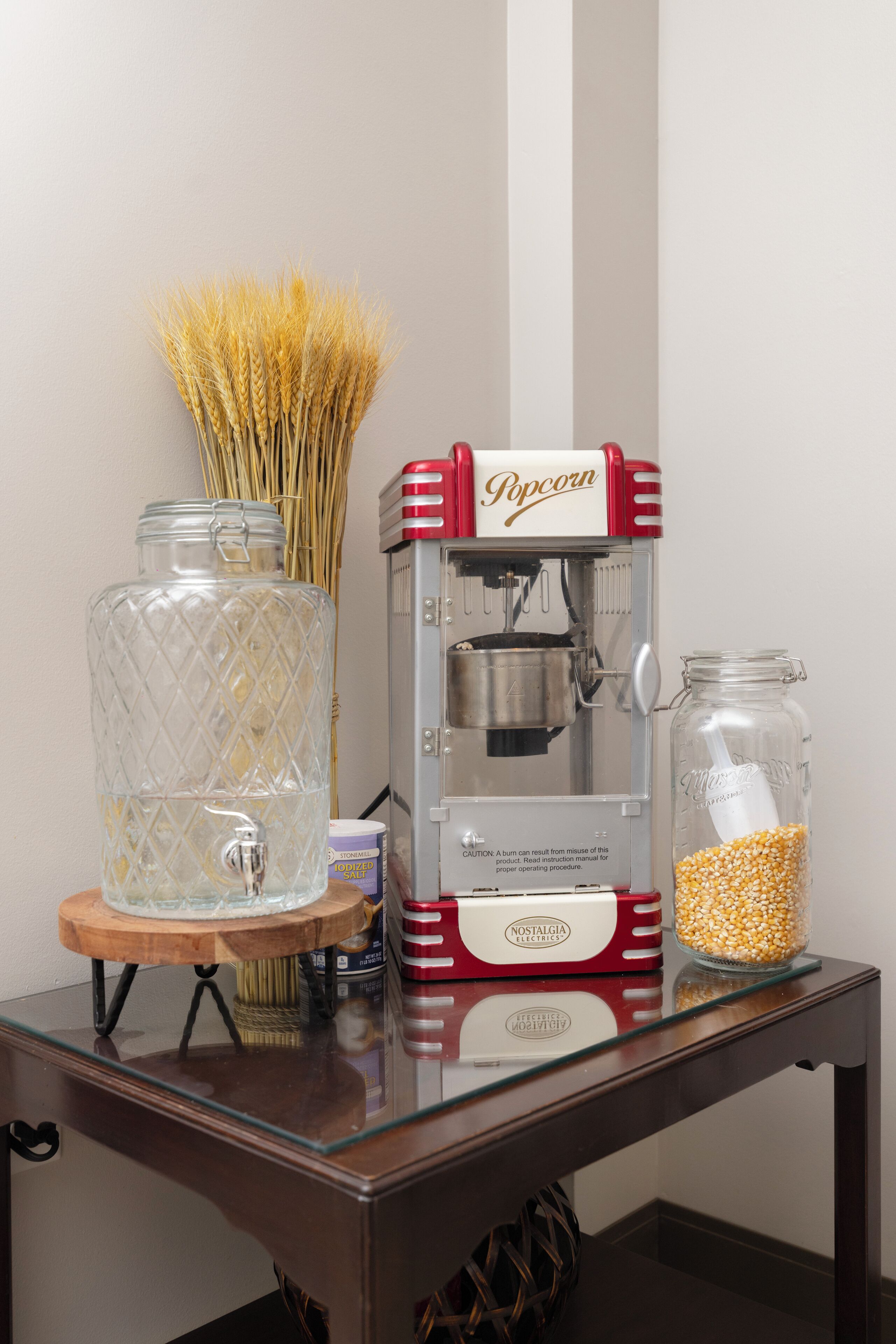 Eine Popcornmaschine, ein Glas mit Deckel und ein Glas mit Popcornkörnern auf einer Holztisch.