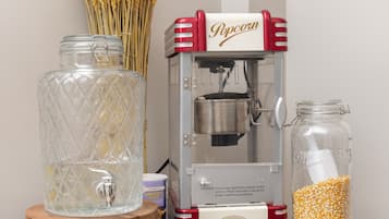 Eine Popcornmaschine, ein Glas mit Deckel und ein Glas mit Popcornkörnern auf einer Holztisch.