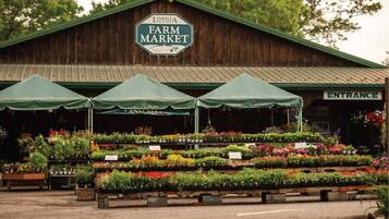 A farm market with a wooden building, green canopies, and various plants on display.