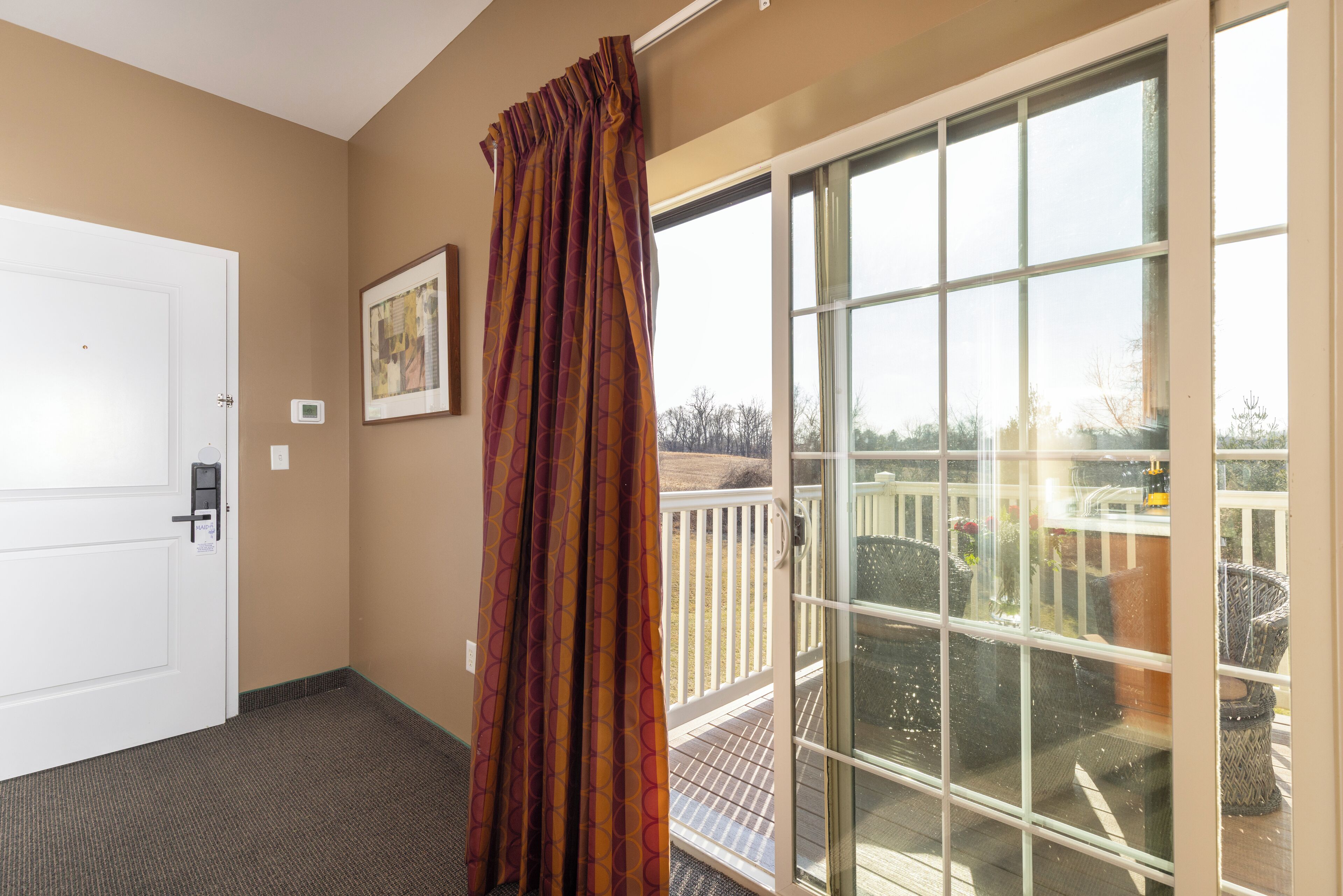 A hotel room with a sliding glass door to a balcony, a white door, and a framed picture on the wall.