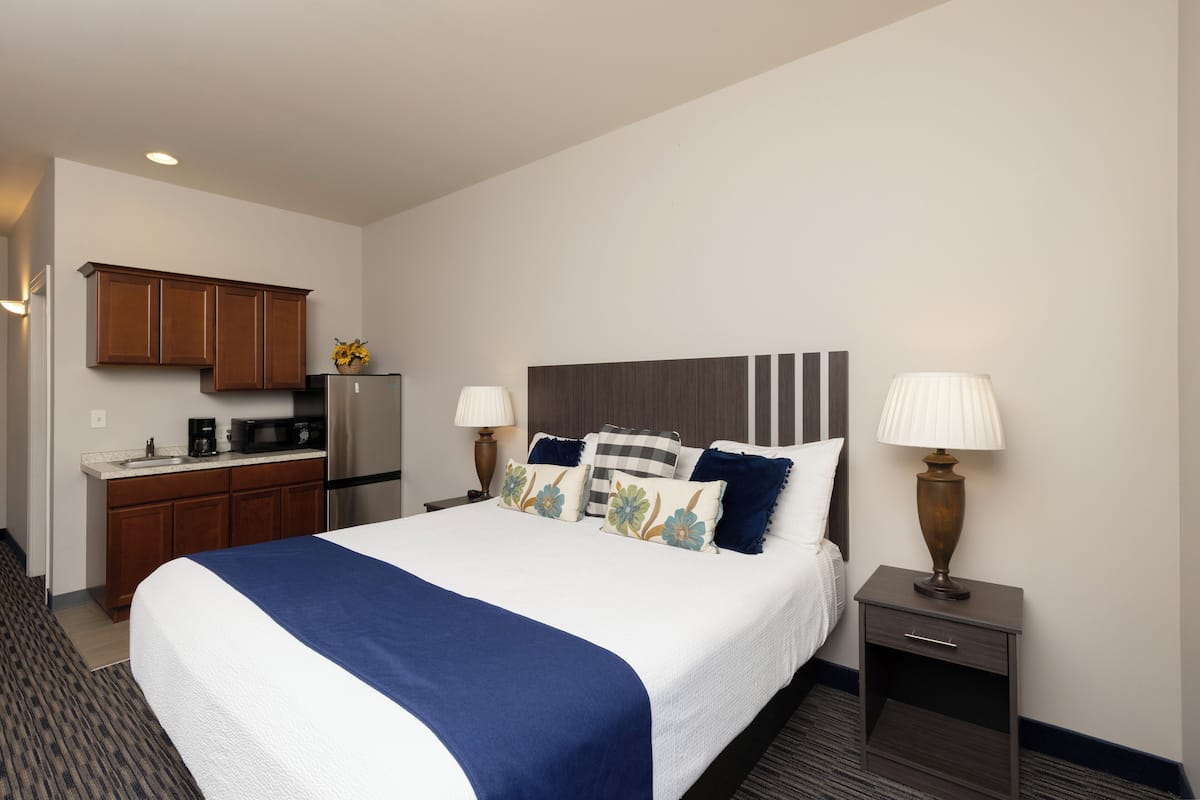 Quarto de hotel com cama, mesas de cabeceira, escrivaninha com frigorífico e micro-ondas.