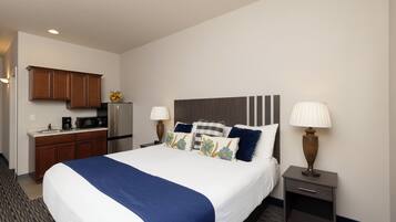 A hotel room with a bed, bedside tables, a desk with a refrigerator, and a microwave.