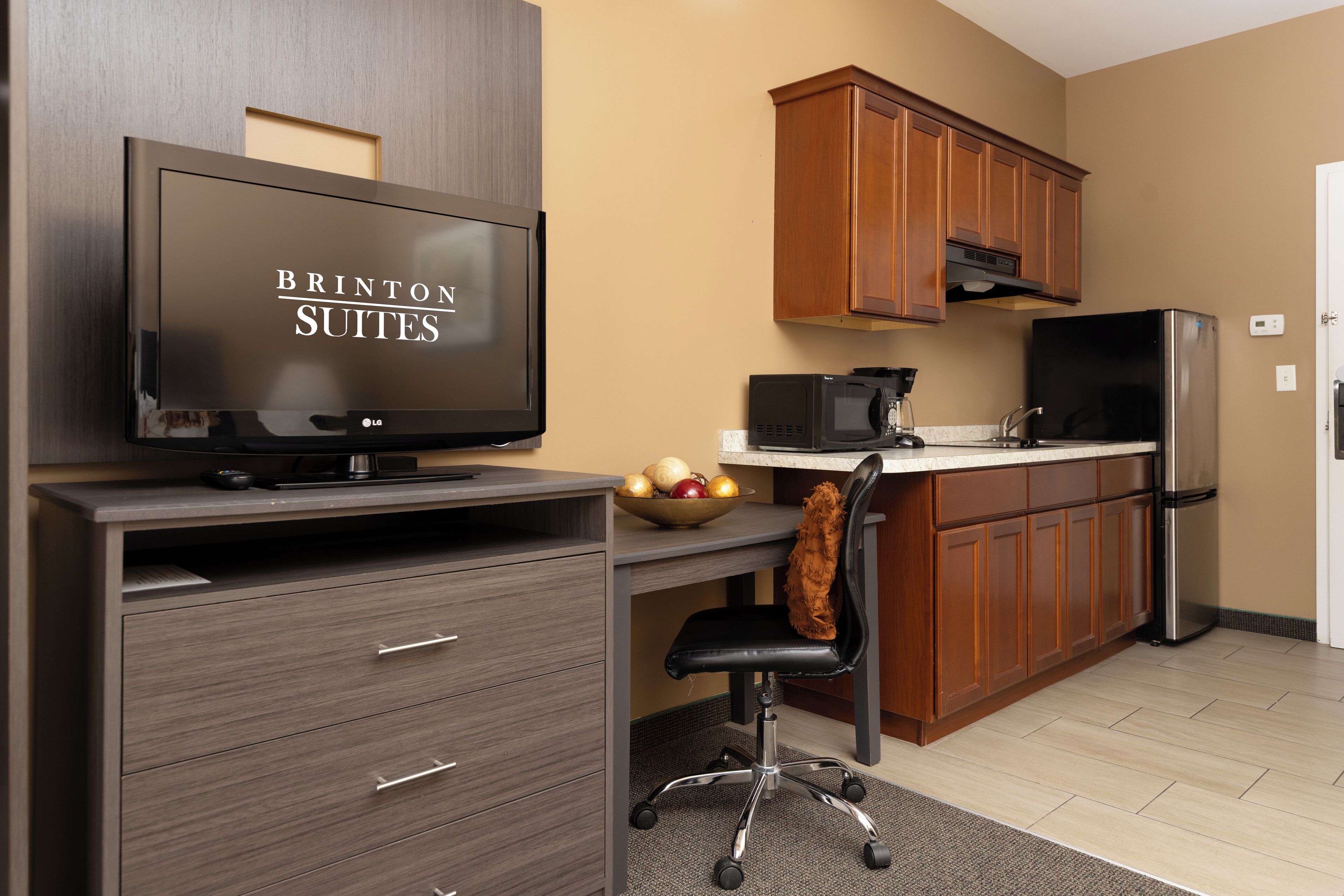 A kitchenette with a microwave, refrigerator, and a bowl of fruit on the counter.