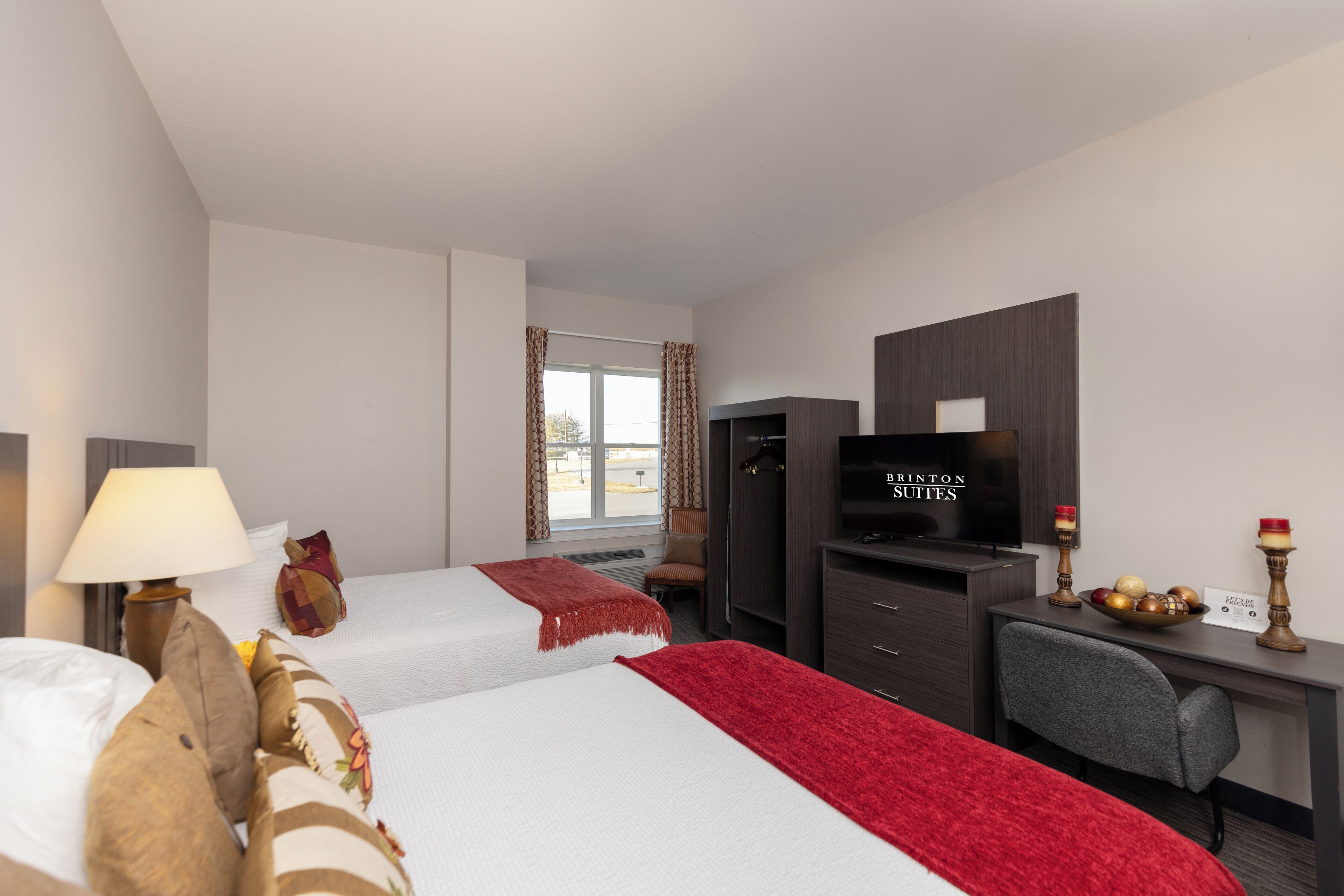 Habitación de hotel con dos camas, un escritorio con televisor, una silla y un ventanal con cortinas.