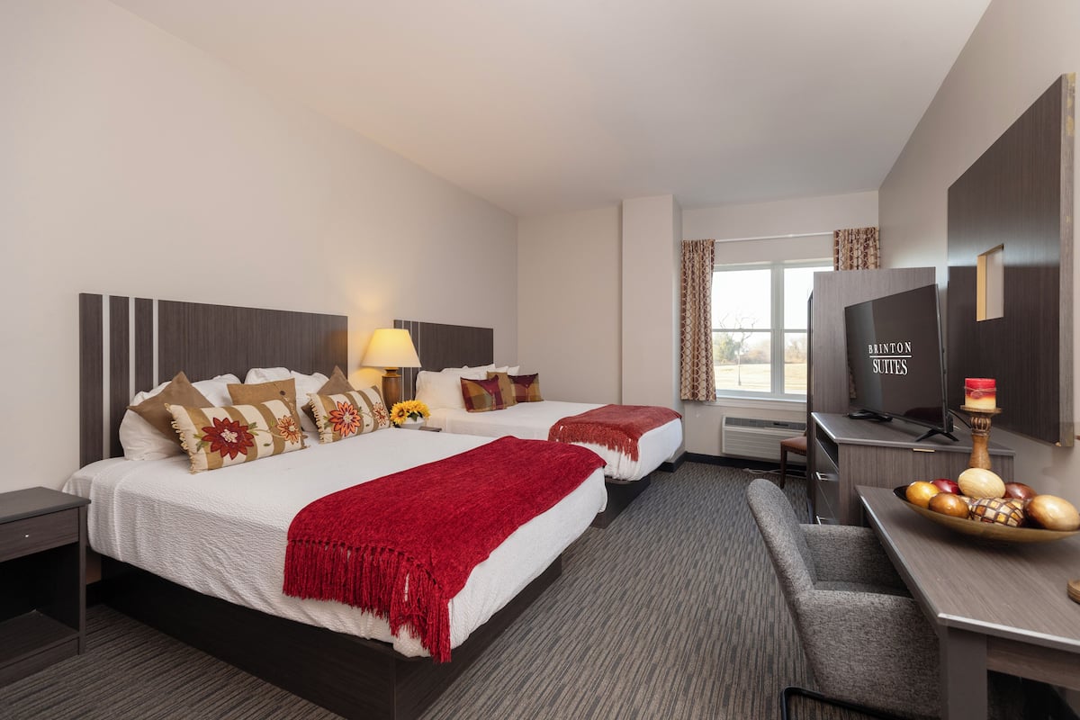 Quarto de hotel com duas camas, uma escrivaninha, uma televisão e uma cesta de frutas.