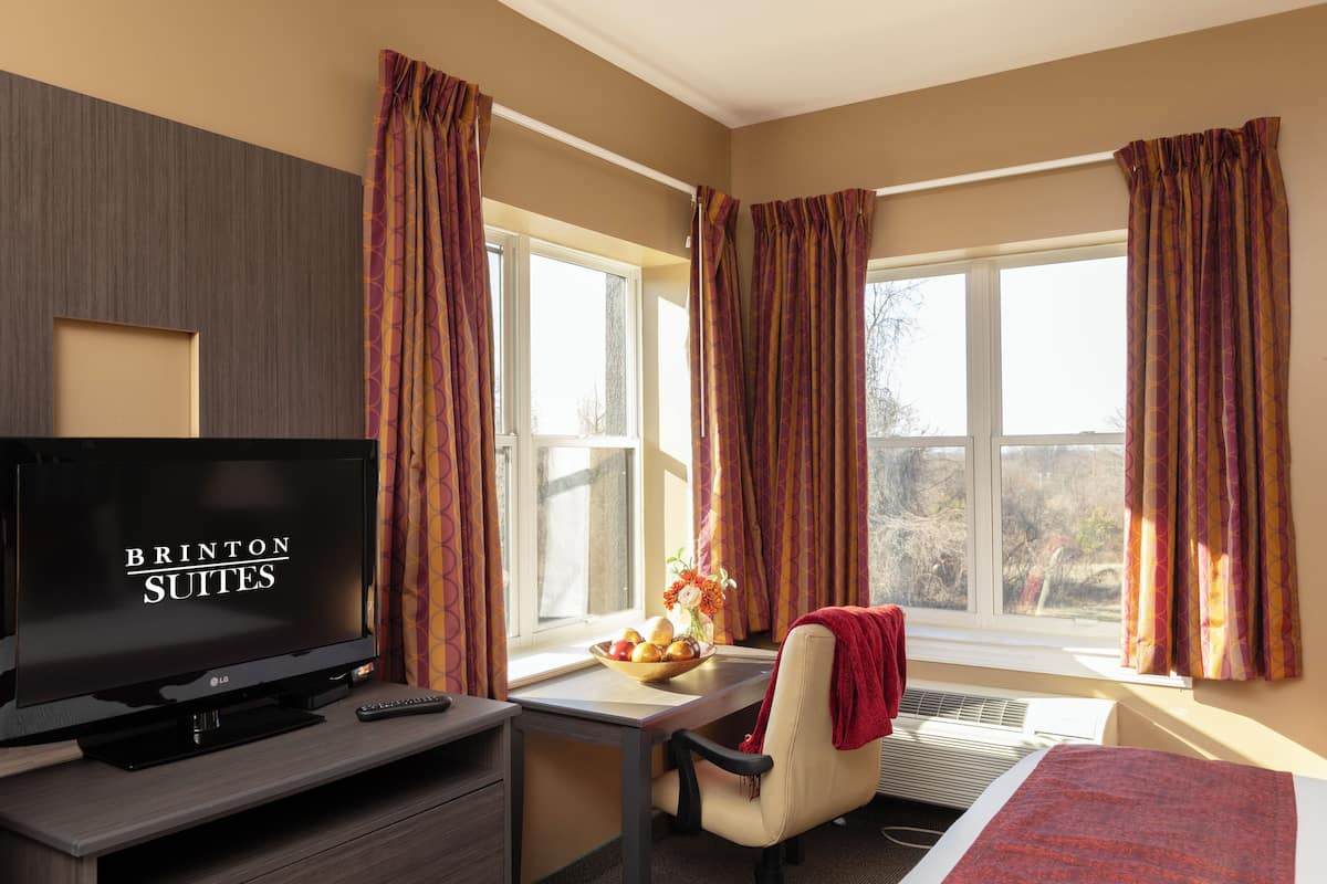 Quarto de hotel com televisão, escrivaninha, cadeira e cama.
