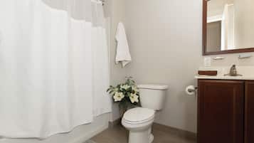 Ein Badezimmer mit Toilette, einer Duschvorhang, einem Handtuch an der Wand, einer Vase mit Blumen und einem Spiegel über dem Waschbecken.
