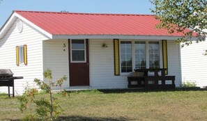 Einbungalow mit rotem Dach, einer Haustür und einer kleinen Veranda mit einer Bank.