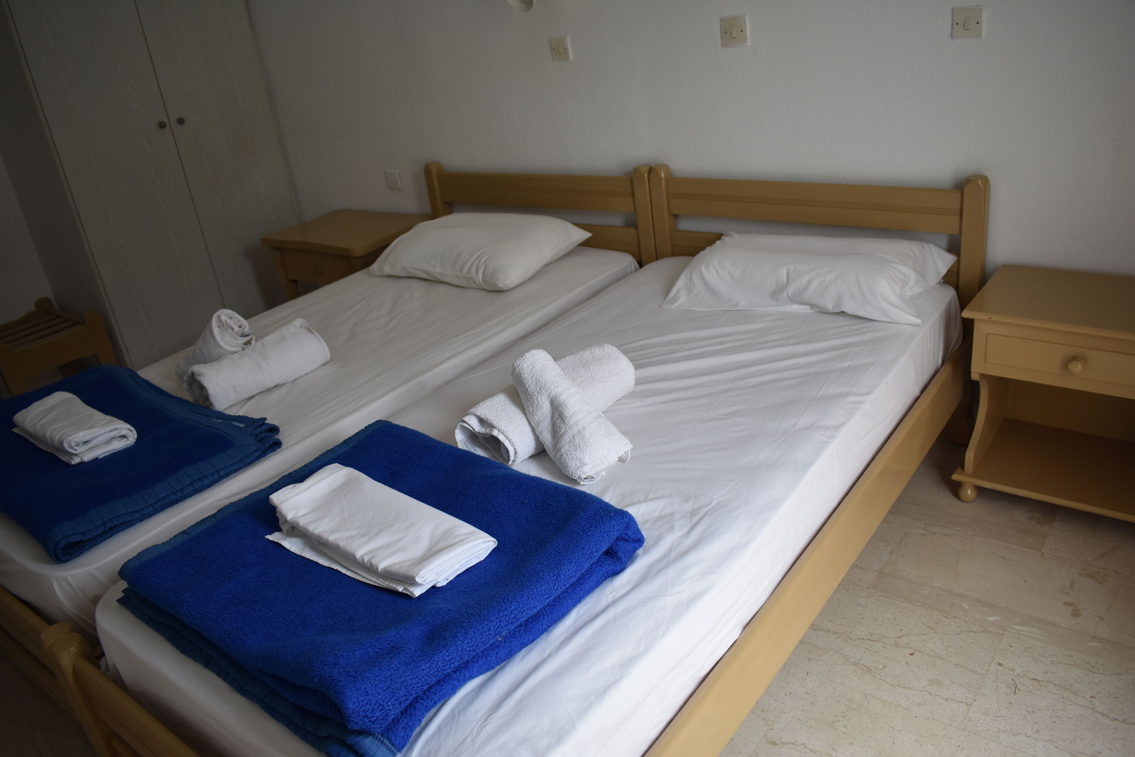 A double bed with white and blue towels, wooden headboard, and nightstands.