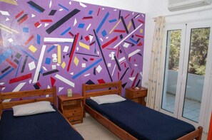 Ein Zimmer mit zwei Holzbetten, einem farbenfrohen Wandgemälde im abstrakten Stil und einer Glastür zum Außenbereich.