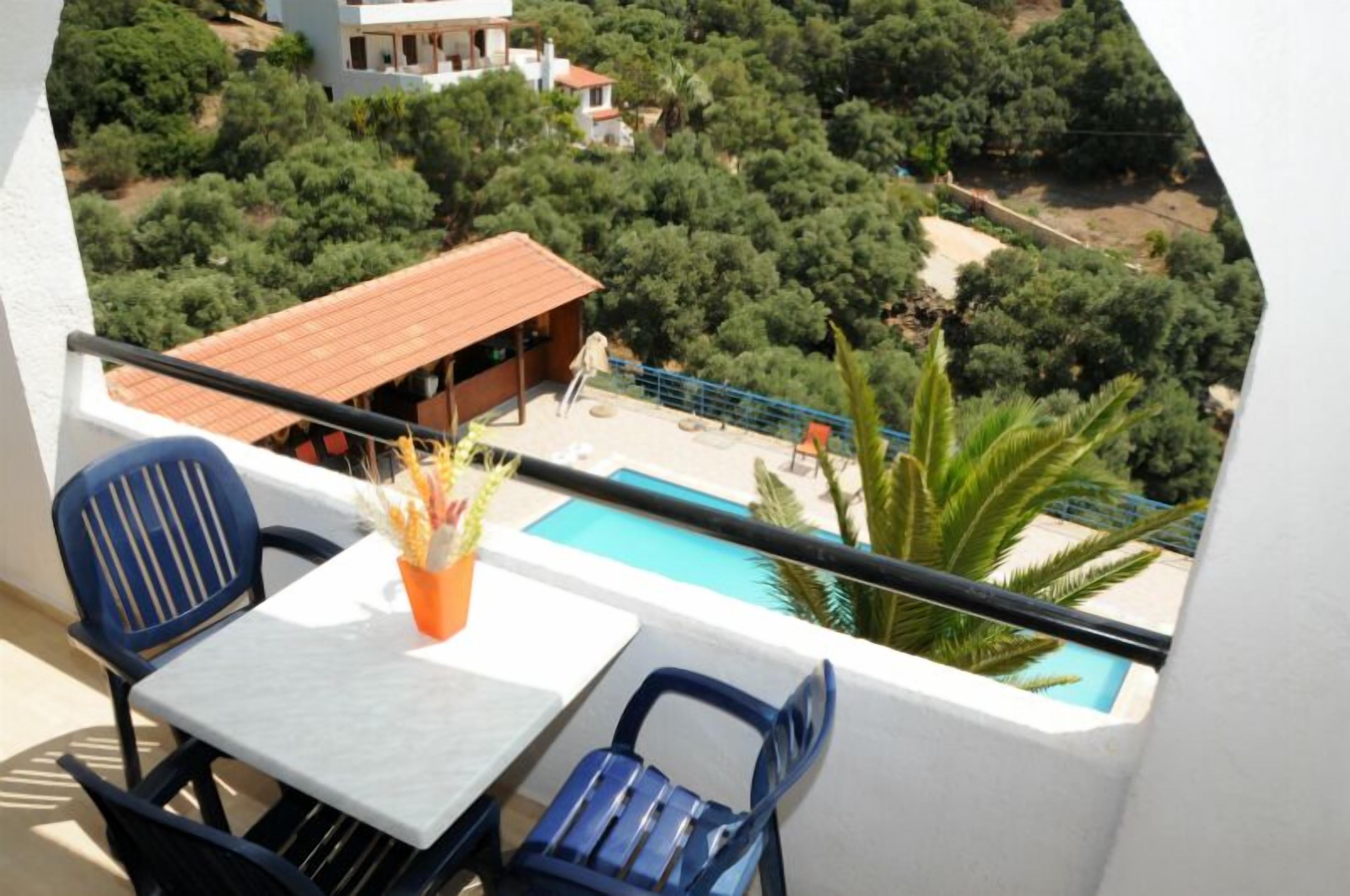 A balcony with a table and chairs, overlooking a swimming pool and lush greenery.