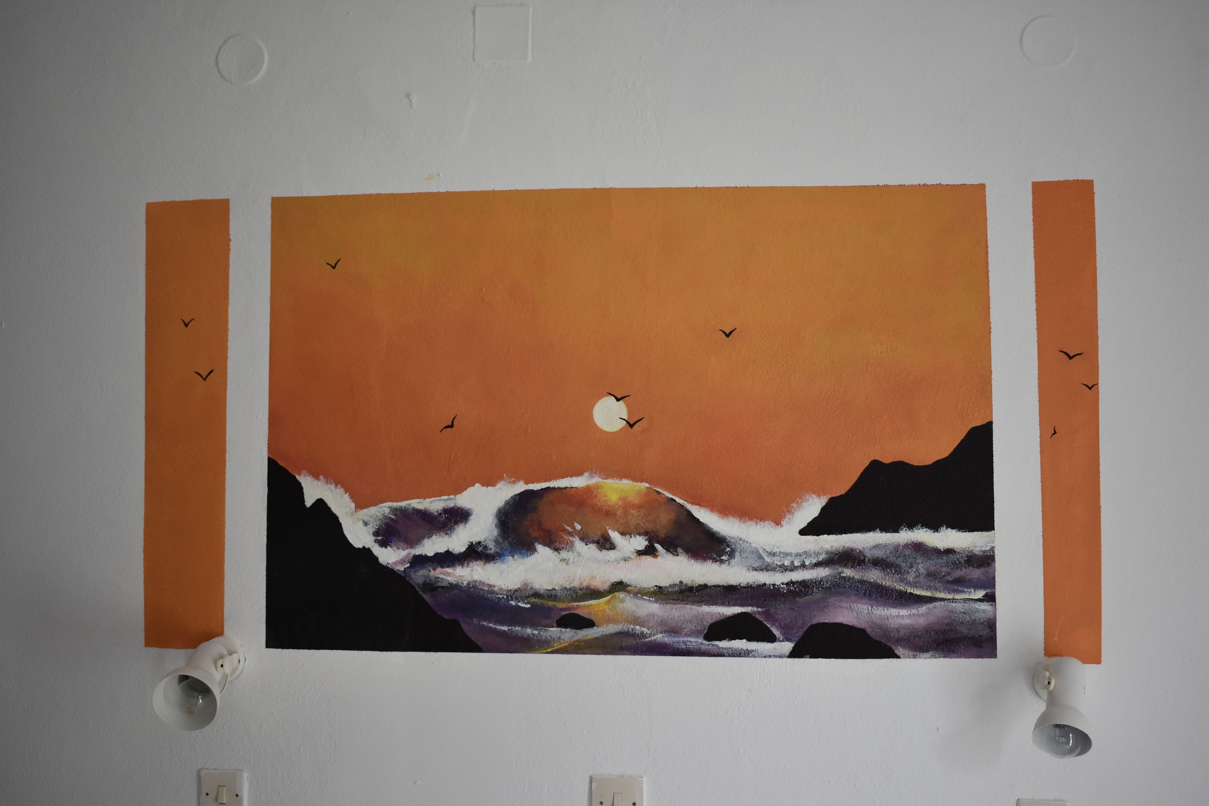 A wall with a painting of a sunset over the ocean, birds flying, and a moon.