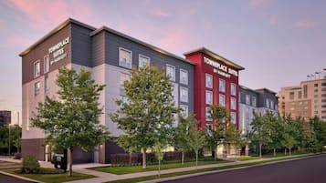 A multi-story hotel with a modern design, featuring a mix of grey and red facades, and a well-maintained landscaped front yard with young trees.