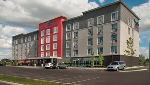 Een hotel met meerdere verdiepingen, een rood-grijs gevel, een parkeerplaats en een heldere lucht.